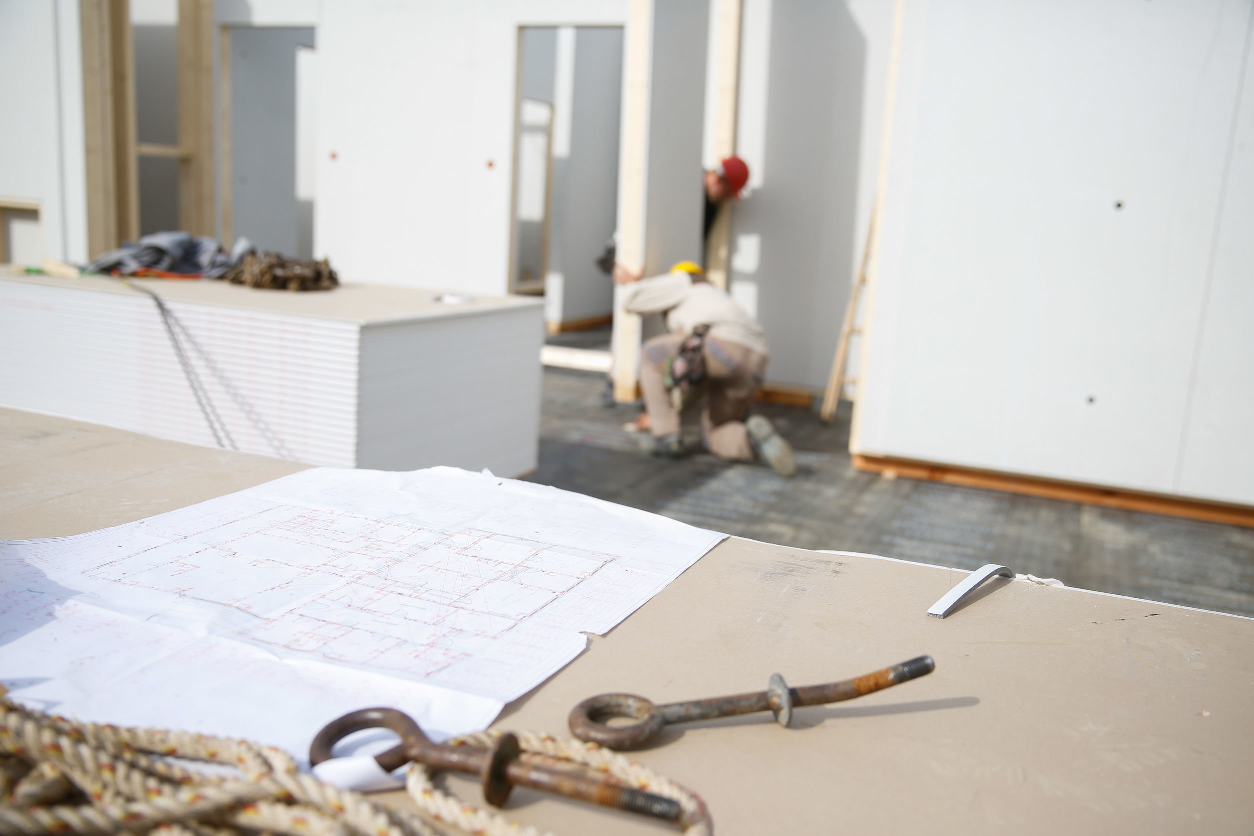 Bauzeichnung und Werkzeug auf einem Tisch und im Hintergrund Schnellbauplatten für den Ausbau