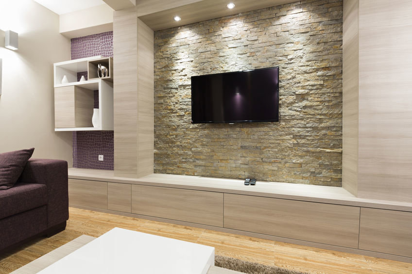Modernes Wohnzimmer mit Regalen und an einer Natursteinwand befestigten Fernseher