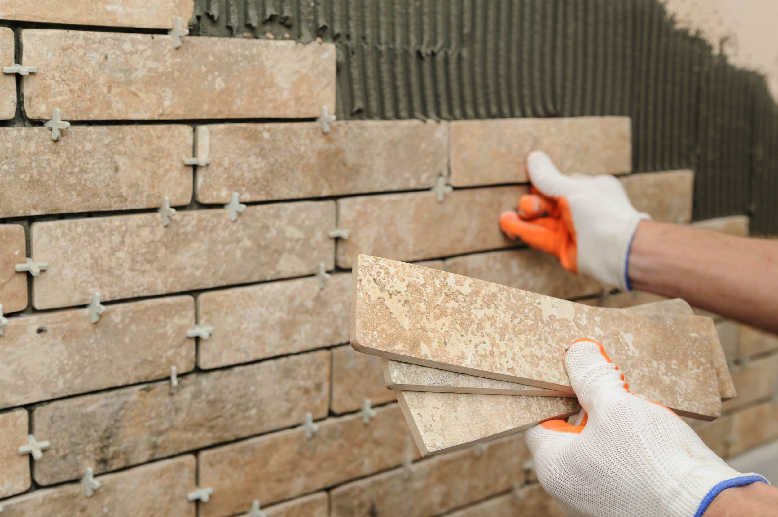 Handwerker drückt Handformriemchen in Klebemörtel an der Hauswand