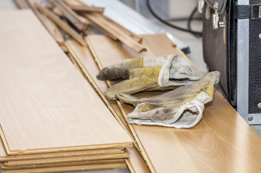 Auf einem Laminatstapel liegen ein Paar Arbeitshandschuhe und Werkzeug