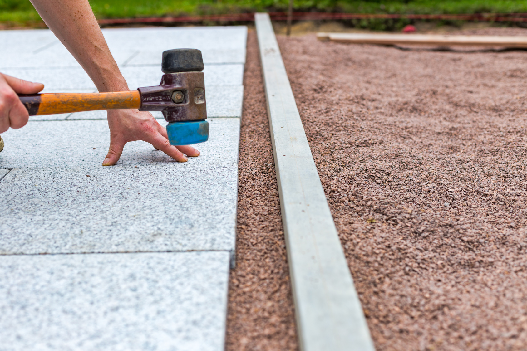 Terrassenfliese wird mit Gummihammer im Kiesuntergrund ausgerichtet