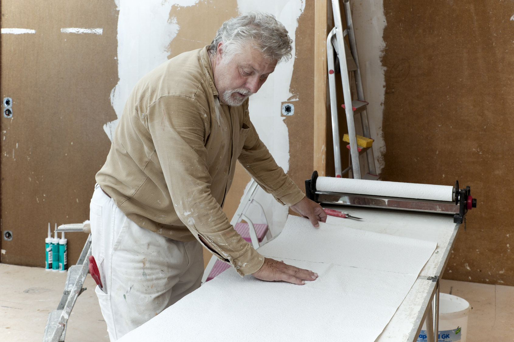 Handwerker steht am Tapeziertisch und bereitet Tapete für das Einkleistern vor